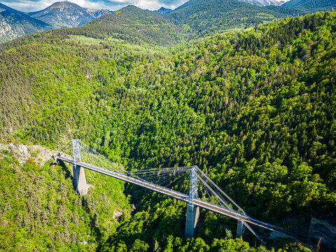 Aerial view of the lofty Gisclard bridge cutting through a verdant valley, a steel thread amidst the lush tapestry of forests, Pont Gisclard, Occitanie, France.