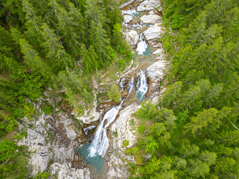 Aerial view of the cascading waterfall cutting through the rugged terrain, surrounded by a vibrant green forest, Vasques de la Lance, Provence-Alpes-Cote d'Azur, France.