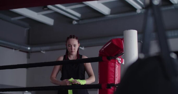 A woman carefully wraps her hands with precision and focus, ensuring maximum protection and support before beginning a rigorous and intense boxing training session in the gym.