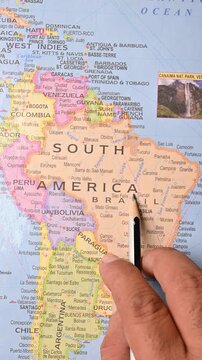 Male Hand with Pencil Pointing at South America on World Map &ndash; Vertical 4K Geography and Travel Concept