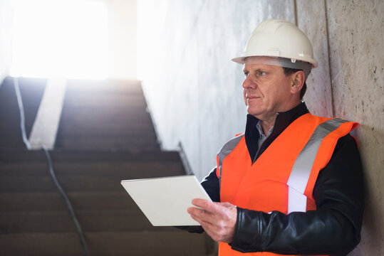 Man with tablet wearing safety vest in building under construction