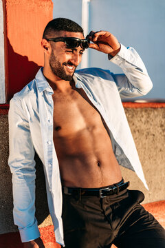 Smiling young man with shirt fully unbuttoned leaning on wall at rooftop