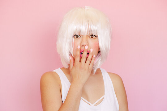 Portrait of frightened young woman with hand covering mouth in front of pink background