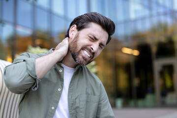 Adult man experiencing acute neck pain, holding his aching neck and shoulder with a pained expression, showing muscle tension and discomfort from stress or long working hours