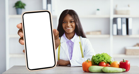 A nutritionist stands in front of a table filled with fresh vegetables and fruits. She holds up a...