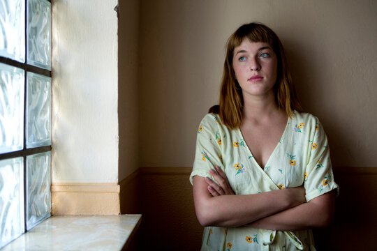 Portrait of serious young woman with arms crossed looking out of window