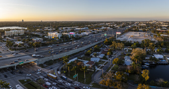 Aerial view of the I-95 freeway cutting through a vibrant urban landscape, with buildings and lush trees bathed in the golden light of the setting sun, Hollywood, Florida, United States.