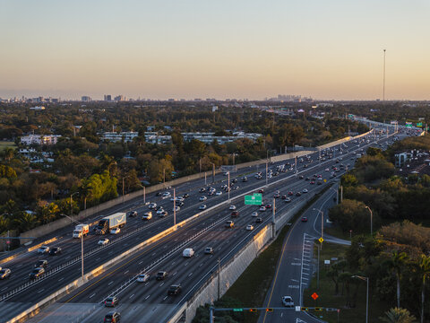 Aerial view of the I-95 highway cutting through a landscape of green trees, with the city skyline on the horizon, Hollywood, Florida, United States.