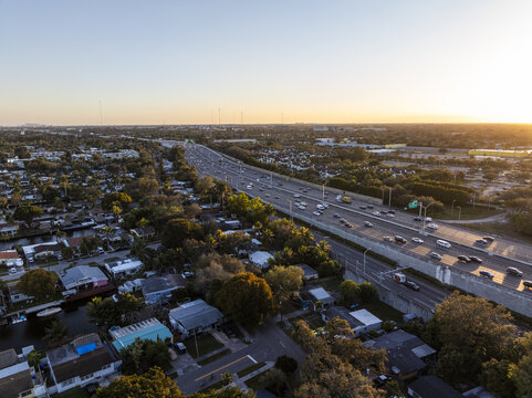 Aerial view of the I-95 highway cutting through a tapestry of suburban homes and verdant foliage under the warm glow of the setting sun, Hollywood, Florida, United States.