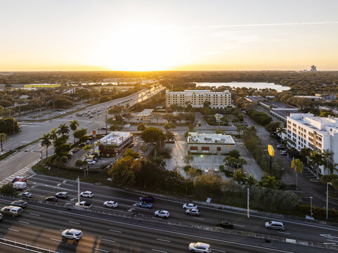 Aerial view of the I-95 highway cutting through the urban landscape with the sun setting behind buildings and a distant lake, Hollywood, Florida, United States.