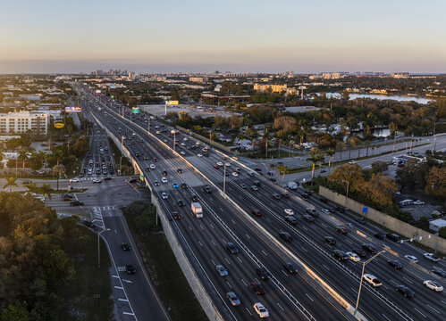 Aerial view of the bustling I-95 highway stretching towards the distant cityscape under a soft, golden sky, Hollywood, Florida, United States.