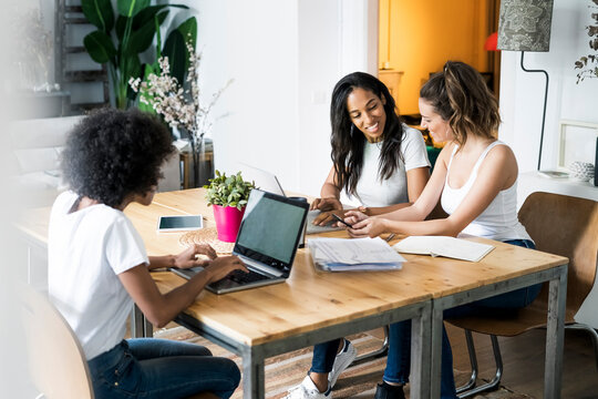 Three women with laptop and documents talking at table