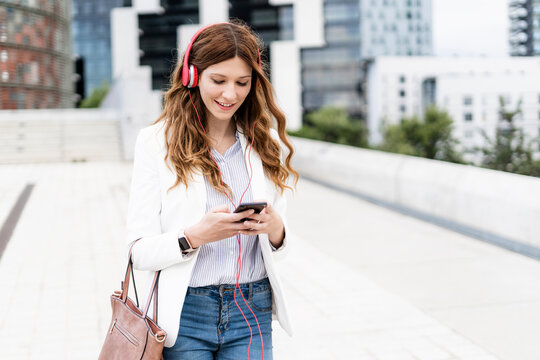 Young businesswoman commuting in the city, using smartphone and headphones
