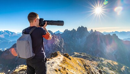 Młody fotograf z plecakiem robiący zdjęcia profesjonalnym aparatem z teleobiektywem na skalistym szczycie góry podczas słonecznego dnia.