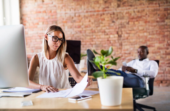 Businesswoman working at desk in office with colleague in background