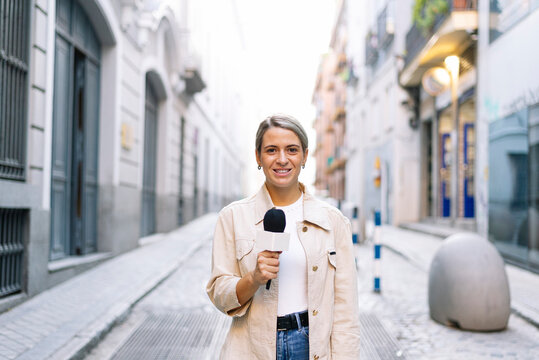 Female journalist talking over microphone while standing on street in city