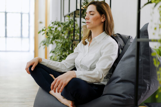 Woman practicing yoga while sitting on bean bag at office