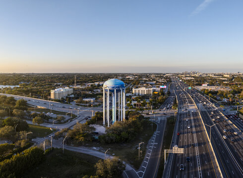 Aerial view of a water tower painted with vibrant blue hues standing tall amidst the sprawling highways and lush greenery, Sarasota, Florida, United States.