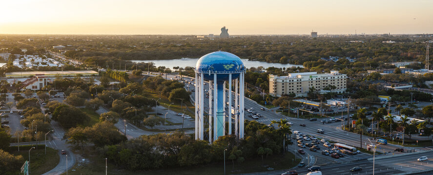 Aerial view of a vibrant water tower with a blue dome stands tall amidst lush greenery, bustling streets, and a golden sunset, Hollywood, Florida, United States.