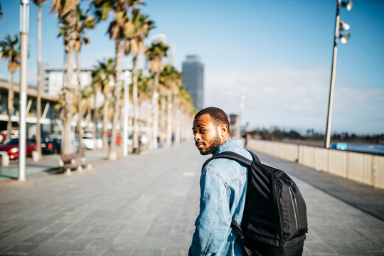 Spain, Barcelona, young man with backpack walking on beach promenade