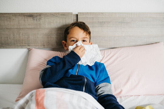 Portrait of sick boy lying in bed blowing nose