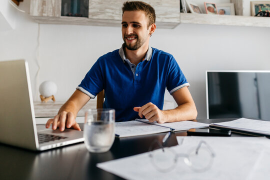 Smiling handsome young man using laptop while doing homework at table