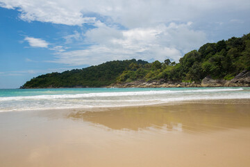 Obraz premium Wide-angle view of a tropical beach in Thailand during a summer morning. In the foreground, the pale sand is wet and reflective, showing the mirror-like surface left by the receding tide.