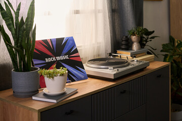 Vinyl record player standing on wooden cabinet next to potted plants and stack of books, colorful...