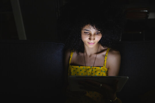 Young woman using her digital tablet in the night on the sofa