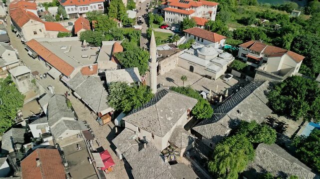 Mostar, Bosnia and Herzegovina - 05 28 2025: Angled drone video of Hajji Kurts Mosque with Hamam Museum to the right and Neretva River in the background in Mostar Old Town on a sunny day.