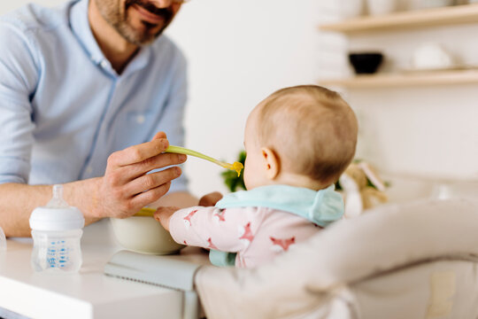 Father feeding baby girl in high chair