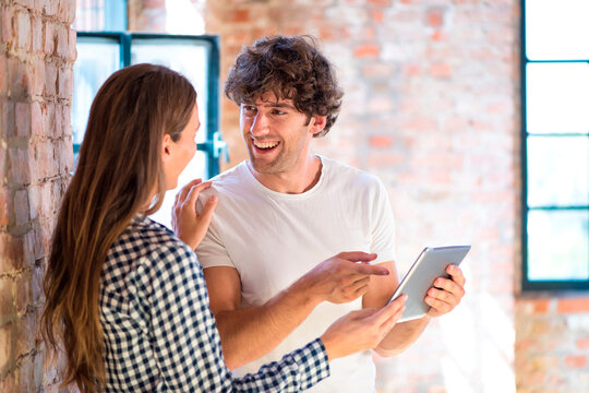 Two young entrepreneurs viewing loft for a start-up company, reading rental contract on digital tablet