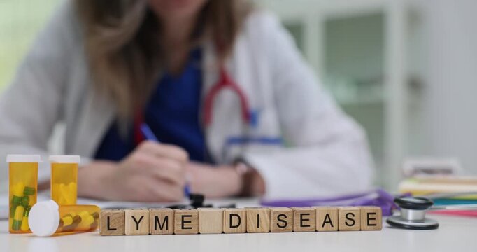 Wooden blocks spell words Lyme Disease on clinic desk. Doctor writes medical notes near pills and stethoscope during infectious disease consultation