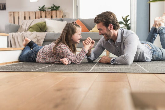 Young man and little girl lying on ground, arm wrestling