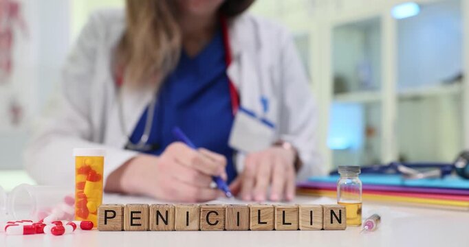 Wooden blocks spell word Penicillin near capsule bottle and vial on clinic desk. Doctor signs prescription sorting tablets for antibiotic course