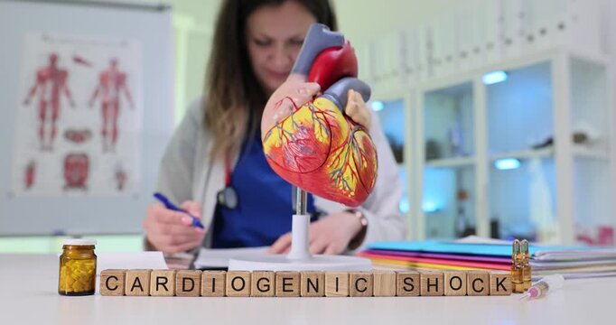 Wooden blocks spell words Cardiogenic Shock near heart model on clinic desk. Doctor writes notes reviewing emergency plan for low cardiac output