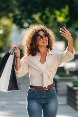 Phone is in hand. Happy woman is with shopping bags in town