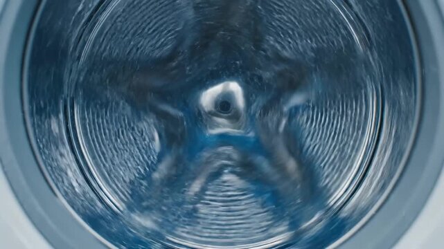 Closeup view inside a clean empty washing machine drum with metallic texture and subtle blue lighting showcasing the perforated surface and central agitator mechanism.