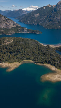 Aerial view of the stunning contrast between the deep blue lake waters and the lush green forests, framed by majestic mountains, San Carlos de Bariloche, Rio Negro Province, Argentina.
