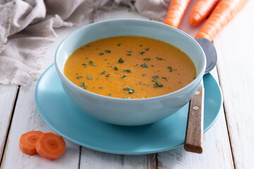 Naklejka premium Creamy carrot soup in blue bowl on white wooden table
