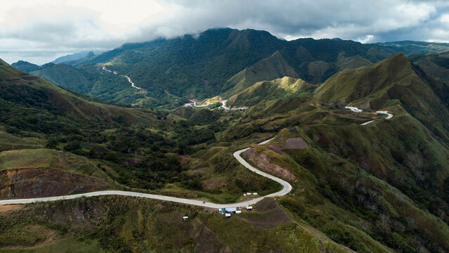 Aerial view of a winding road snaking through the rugged, verdant mountains under a sky touched with soft clouds, Igtuble, Tubungan, Philippines.