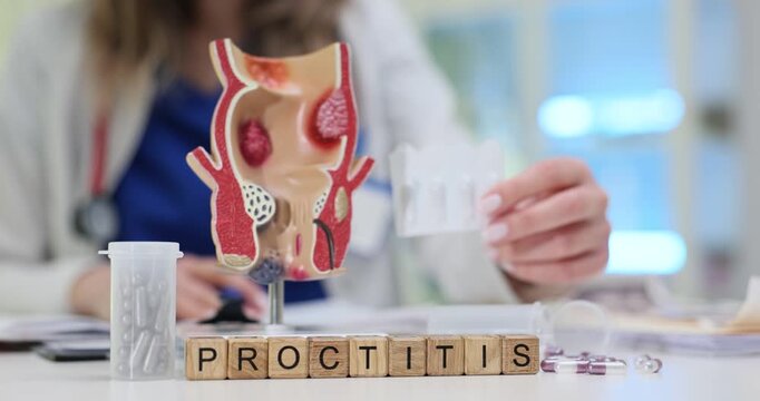 Wooden blocks spell word Proctitis near rectum anatomy model and medicine pack. Doctor holds white blister pack recording symptoms for therapy plan