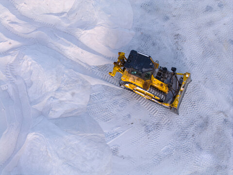 Aerial view of a yellow bulldozer pushing through a pristine white landscape, its tracks carving a path through the untouched terrain, Aigues-Mortes, Occitanie, France.