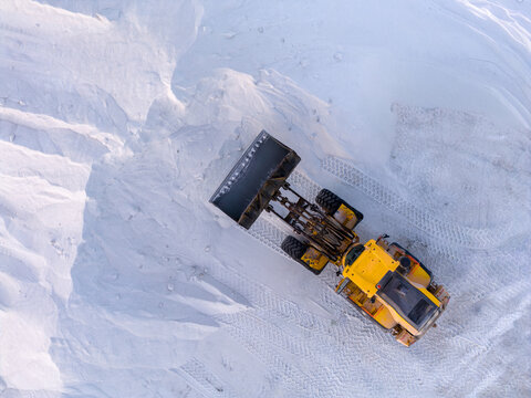 Aerial view of a yellow bulldozer amidst a sea of white salt mounds, a stark contrast under the clear sky, Aigues-Mortes, Occitanie, France.