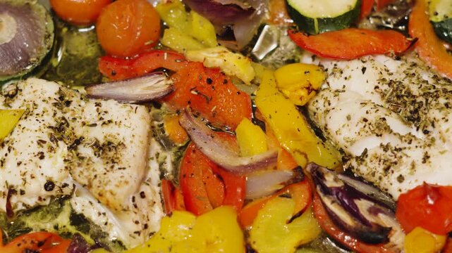 Slow pan over cooked traybake of wild caught atlantic Cod fillets in bubbling olive oil with mediterranean diet vegetables. Peppers, onions, courgette, tomatoes. Healthy dinner food.
