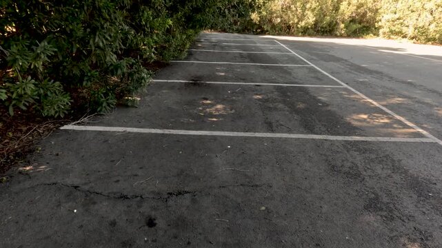 A person walks along a sidewalk with sunlight and shadows mixing on the ground. The surface has marks and patches, creating an interesting view in the afternoon.