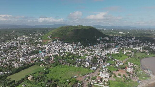 High aerial drone over Bheemili coastal town and prominent green hill, Visakhapatnam, Andhra Pradesh, India.