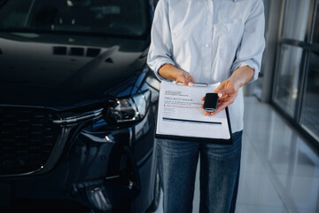Front view of woman that is giving documents to sign in to buy a new car in the showroom
