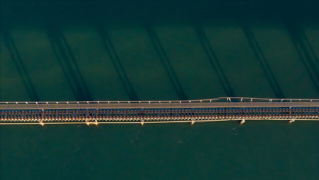 Aerial view of a bridge stretching across the water, shadows dancing on the surface, creating a mesmerizing contrast of light and dark, Knysna, Western Cape, South Africa.
