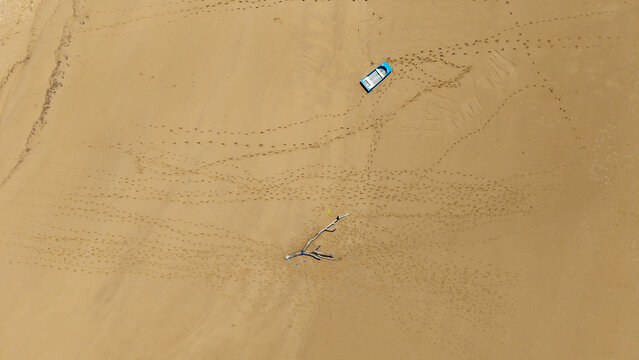 Aerial view of a lone boat sits on the vast expanse of sandy terrain, footprints scattered like whispers across the ochre surface, Plaatjie, Eastern Cape, South Africa.